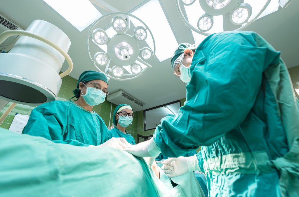 Drei Personen in grüner Kleidung stehen um einen Operationstisch herum.